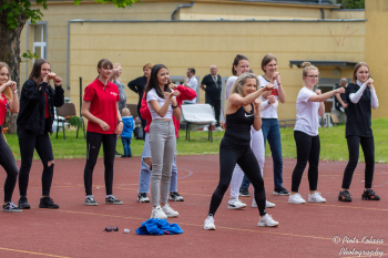 Zdjęcie przedstawia uczniów ćwiczących na boisku szkolnym z instruktorką fitness.
